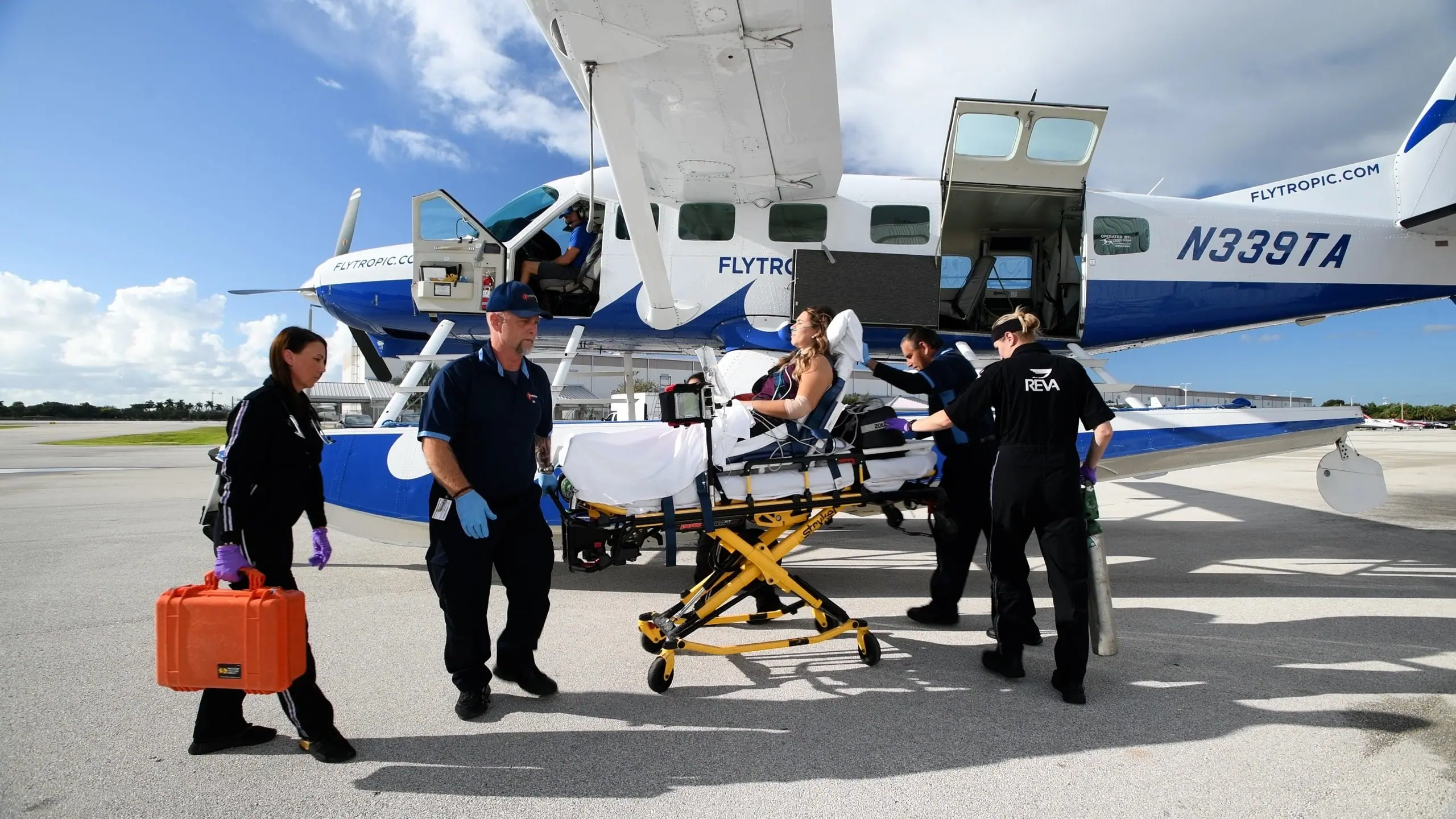 a woman on a stretcher in front of a plane that says flytropic.com on the side